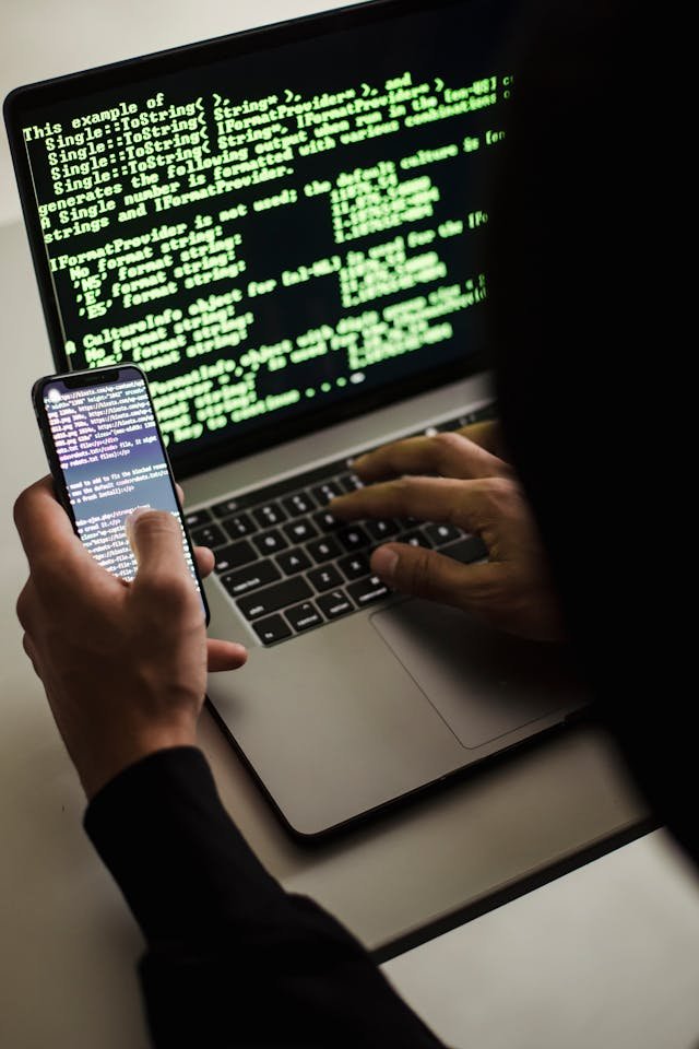 A software expert witness with smartphone typing on laptop at desk