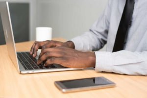person-wearing-white-dress-shirt-and-black-necktie-using-macbook-air-on-beige-wooden-table
